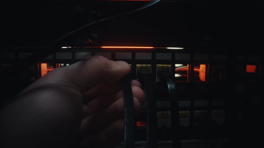 A technician's hand plugs an ethernet cable into a patch panel in a dark, glowing server room
