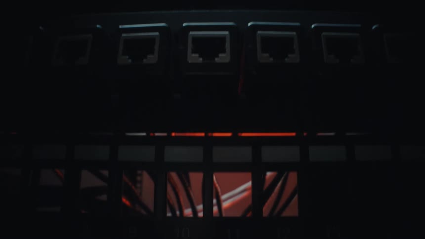 A dramatic close-up pans down the intricate wiring and blinking indicator lights of a server rack in a dark data center