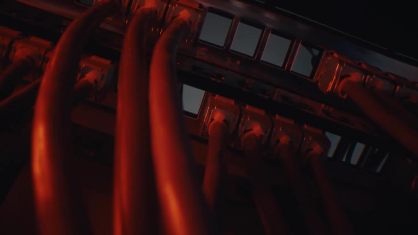 A dramatic close-up of network cables plugged into a server rack, illuminated by a moody red light in a dark room