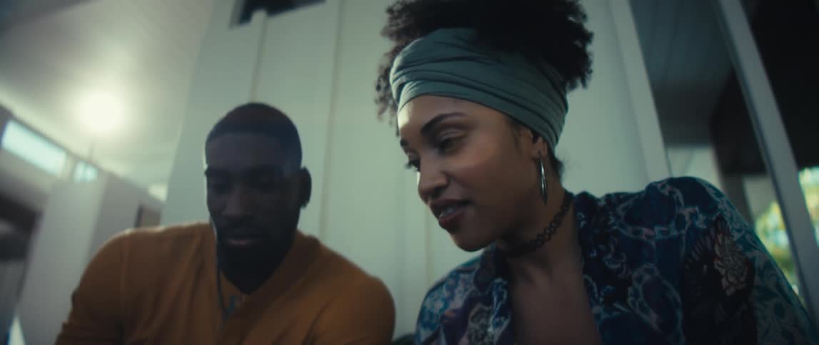 A low-angle shot pulls back to reveal a young African American couple smiling while browsing on a tablet together at home