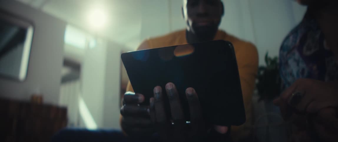 A low-angle close-up of a man holding a tablet computer while sitting with a companion in a brightly lit room