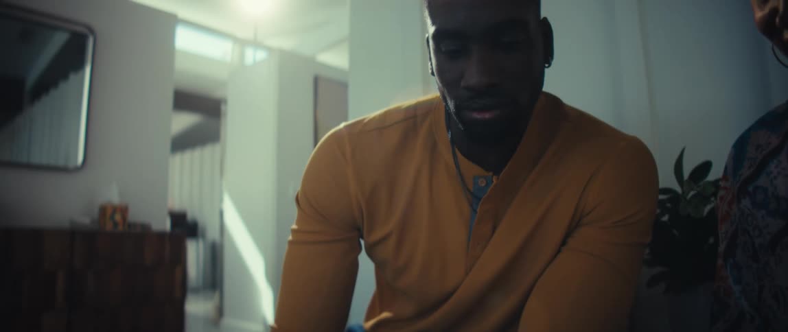 Slow focus pull from a tablet to a contemplative Black man sitting in a brightly lit modern home