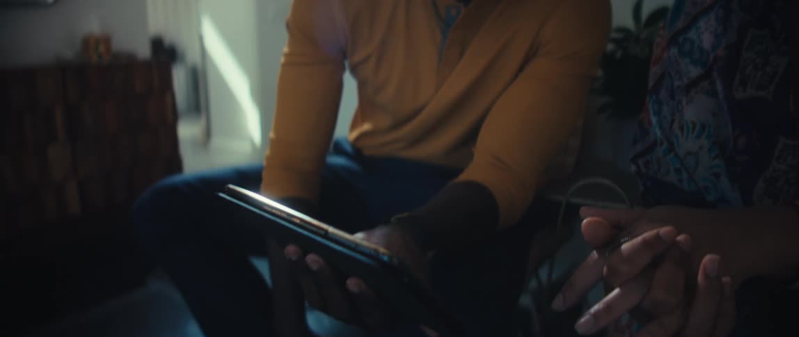 A young couple sits together in a sunlit room, attentively looking at a digital tablet