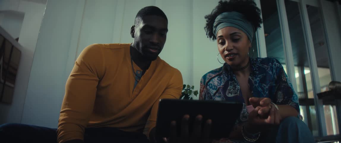 Low angle slow motion push-in shot of a young Black couple sitting together and excitedly discussing something on a digital tablet