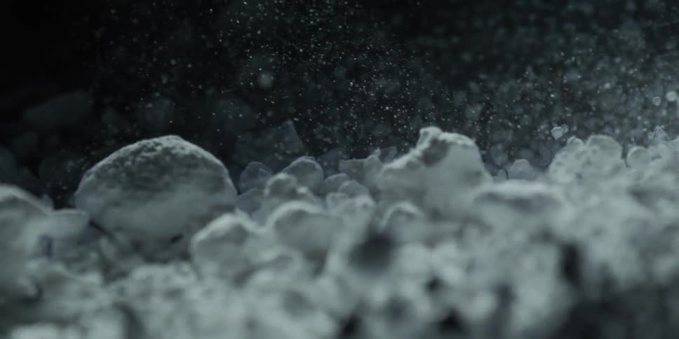 A mesmerizing slow-motion, close-up shot reveals white crystalline powder settling against a dark background