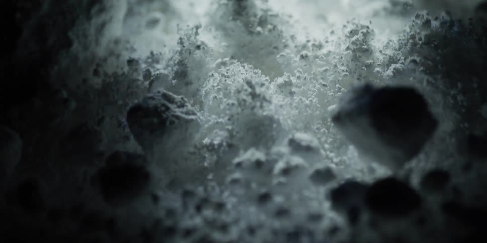 A dramatic macro shot travels through a mysterious, textured white powder resembling a desolate, rocky landscape