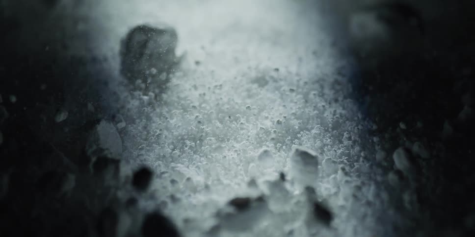 A dramatic macro shot captures a mysterious white powder bubbling and dissolving in slow motion