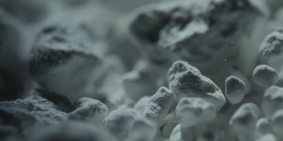 An extreme close-up of a mysterious white, clumpy powder is slowly revealed by a moving light source in a dark setting