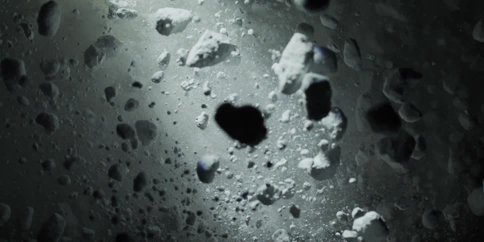Ethereal white rocks and dust particles float and expand in zero gravity against a dark backdrop