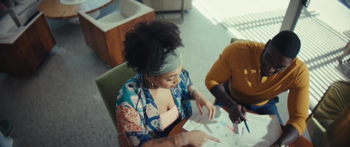 A high-angle shot of a young Black couple happily planning their finances together at a table in their modern home