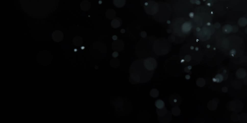 Slow motion macro shot of delicate snow particles gently falling against a black background