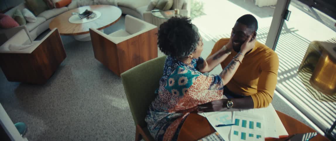 A loving couple embraces and kisses while reviewing their finances together in their stylish, sun-drenched home
