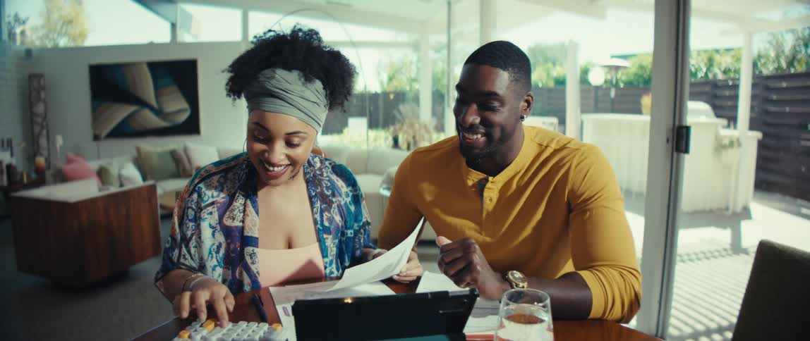 Slow pull-out shot of an excited young couple happily working on their household budget together at their dining room table