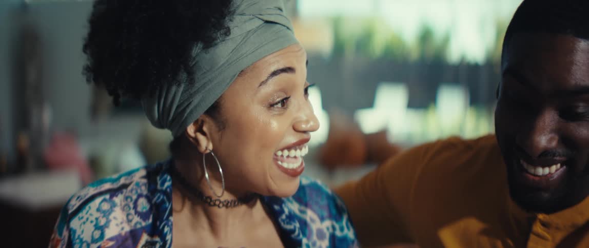 A joyful African American couple shares a laugh in their sunlit living room, their faces filled with happiness and love
