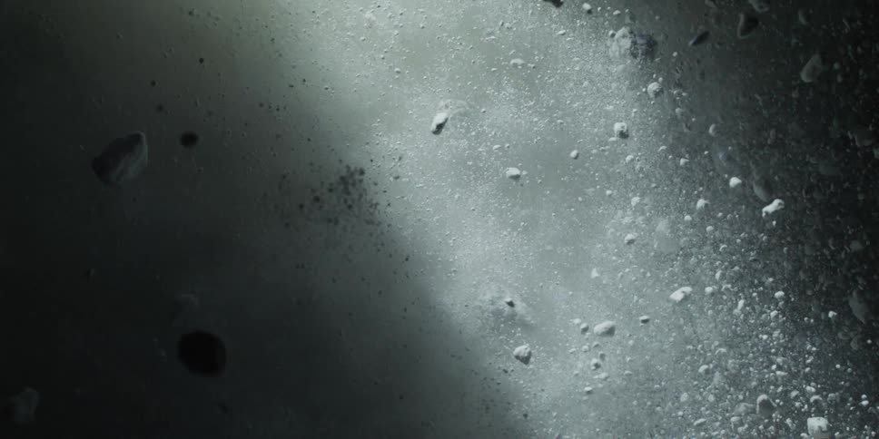A dramatic slow motion close-up of white particles and rocks falling through the dark