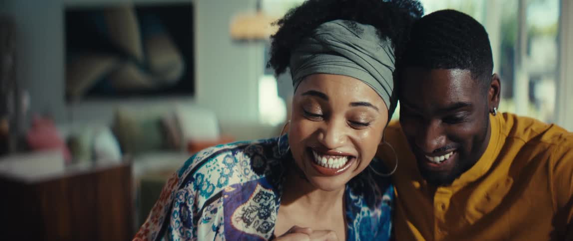 A stylish young woman expresses pure joy and excitement as she laughs with her smiling partner in their bright living room