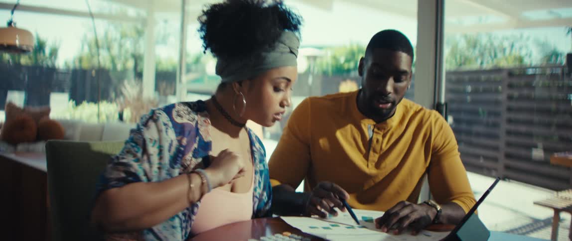 A young couple sits together at their dining table, seriously reviewing financial documents and planning their household budget