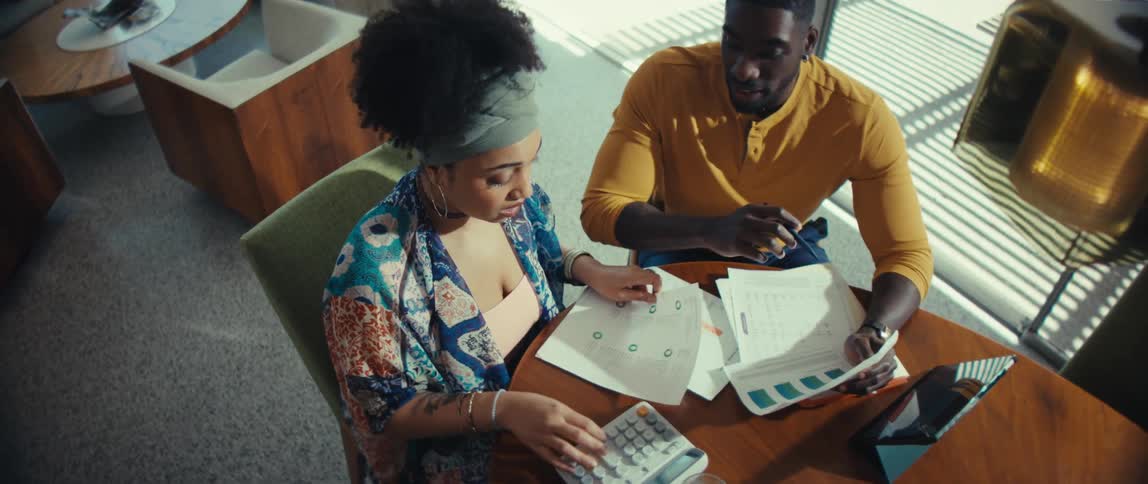 A high angle shot zooms into a young couple planning their finances together at the dining table in their modern, sunlit home