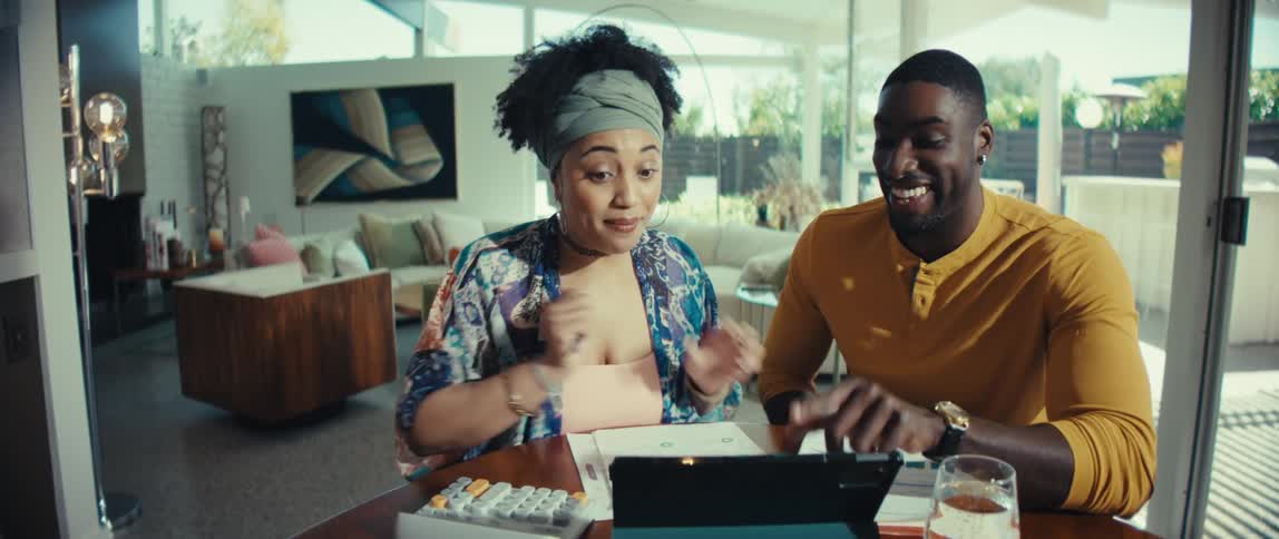 An excited young Black couple receives great financial news on their tablet and happily celebrate together with a hug and kiss in their modern home