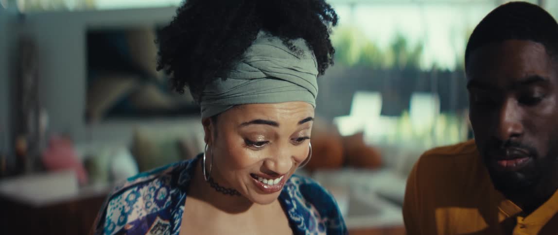 A beautiful young woman with a headwrap smiles and laughs excitedly while looking down at something in her home