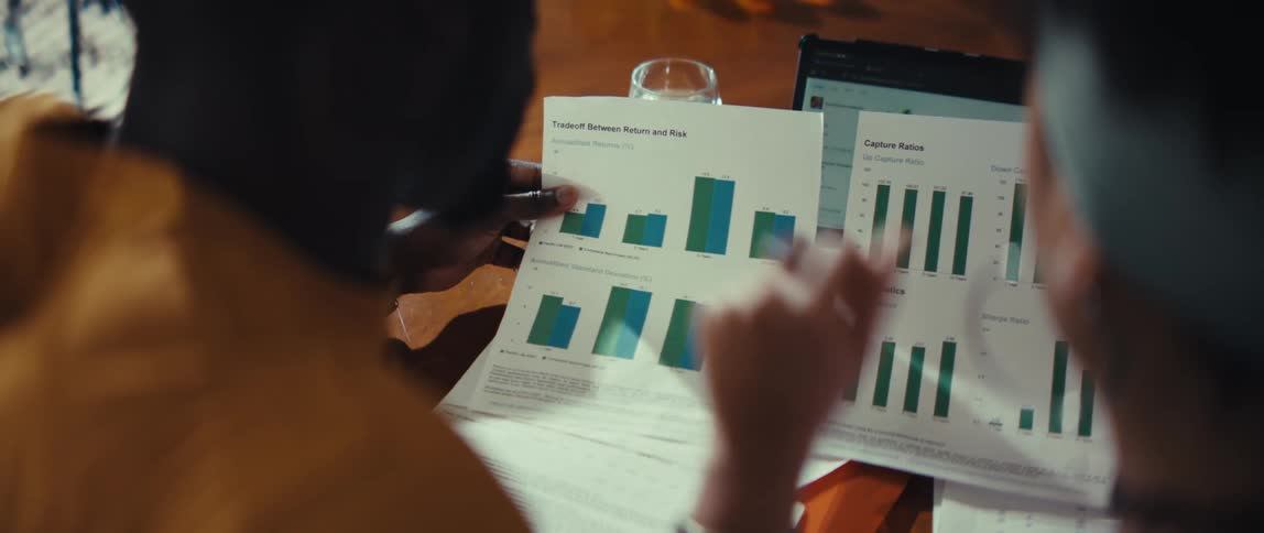 Over-the-shoulder shot of two diverse colleagues analyzing business performance graphs and charts during a meeting