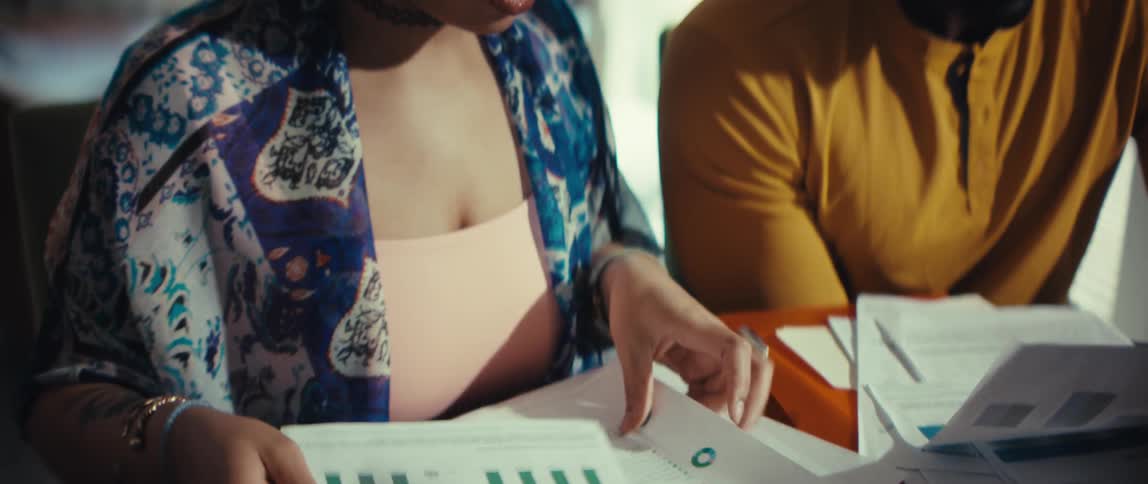Close up slow motion shot of a woman reviewing financial charts and documents with her partner at a table with a calculator