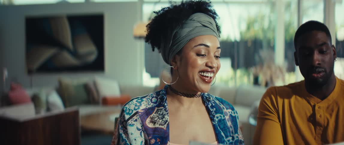 A stylish young woman expresses joyful surprise and laughter during a collaborative discussion at home