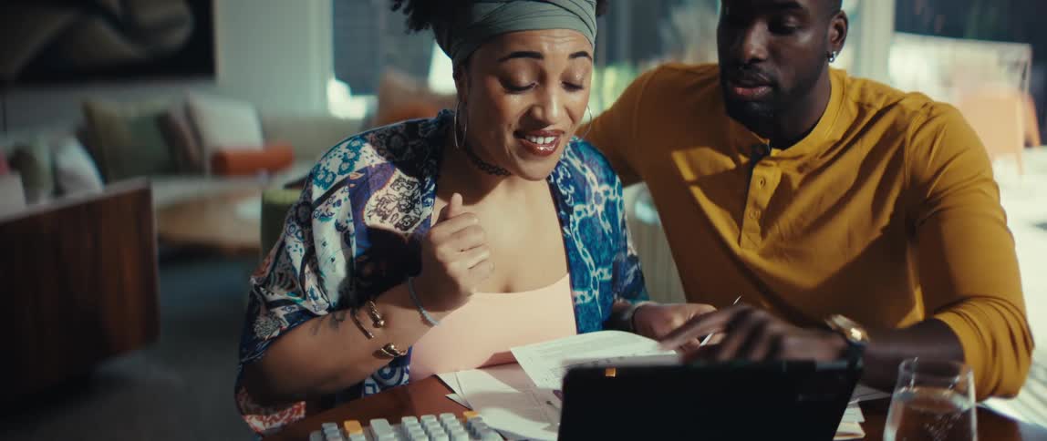 An excited young woman reacts with surprise and happiness while doing finances with her partner at home in slow motion