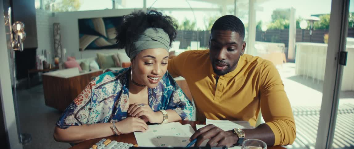 A young Black couple works together to manage their finances, discussing documents and using a calculator at home