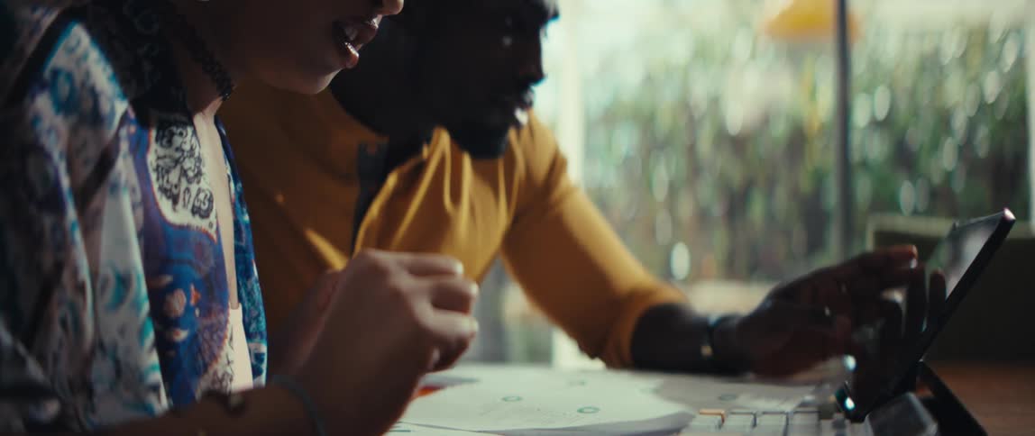 A young Black man and woman collaborate on a tablet in a bright space, smiling and clapping in celebration of their success