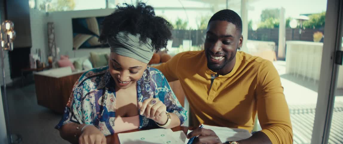 An excited and happy Black couple celebrates good financial news, hugging and dancing after reviewing their budget at their modern home