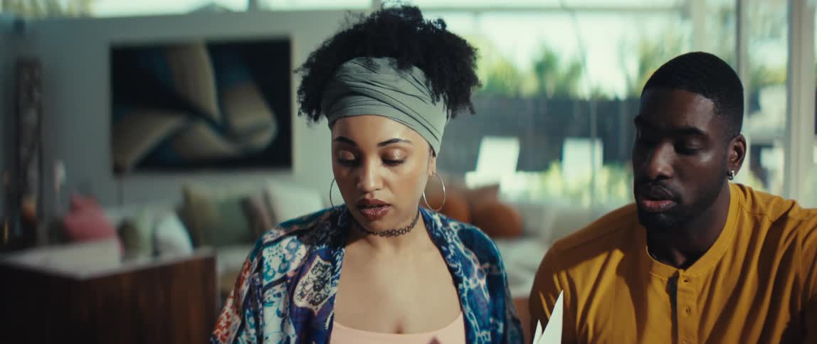 A young couple reviews financial documents together at home, and the woman's expression changes from serious to joyful upon reading good news