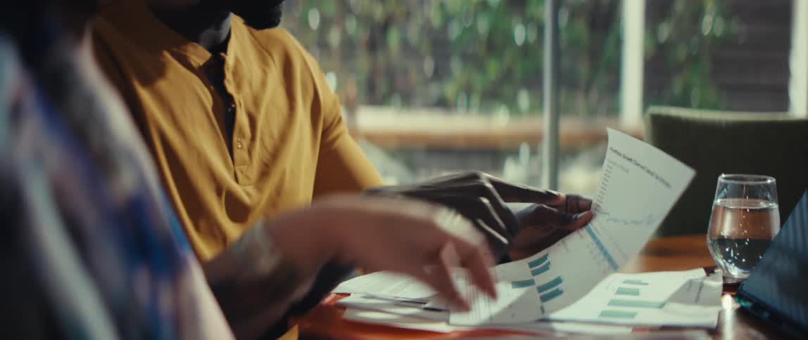 A diverse business team's hands are shown in slow motion as they collaborate and analyze financial reports with charts and graphs