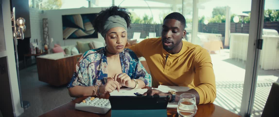 A stylish young couple collaborates on their household finances, using a tablet and calculator to review bills at their dining table