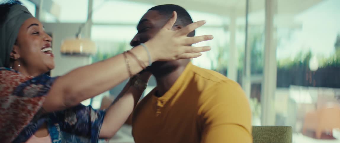 A joyful African American couple celebrates good news, laughing and kissing while sitting at the table in their modern home
