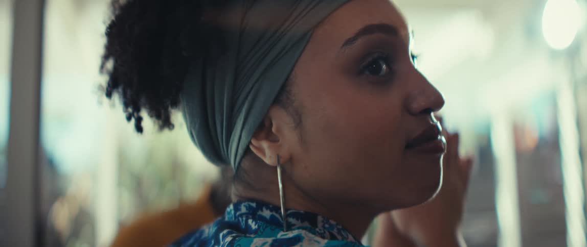 A stylish young woman with a headscarf and hoop earrings smiles and listens intently in a sunlit room