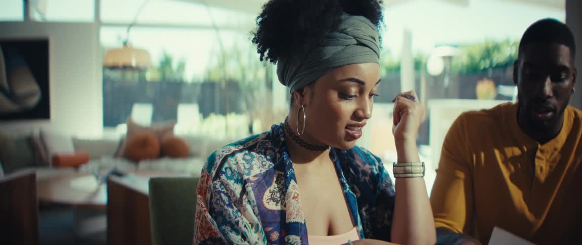 A young Black couple happily calculates their finances together at the dining table in their sunlit modern home