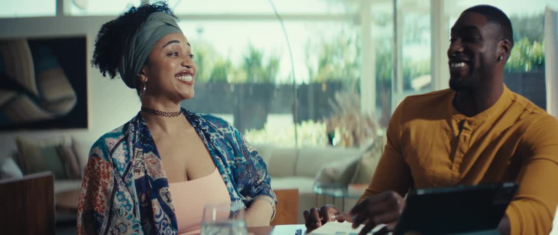 A happy couple celebrates good news together, laughing and kissing while looking over documents at their dining table in a sunlit modern home