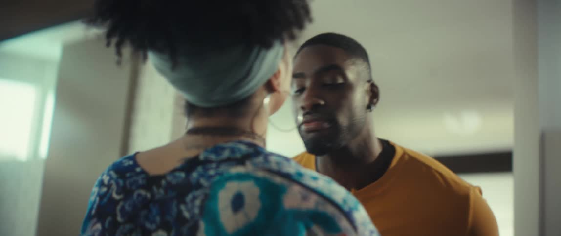 An affectionate African American couple playfully kiss and then smile as they hold hands at home