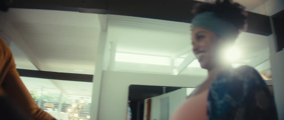 An affectionate pregnant couple smiles and dances lovingly in slow motion inside their bright, sunlit home