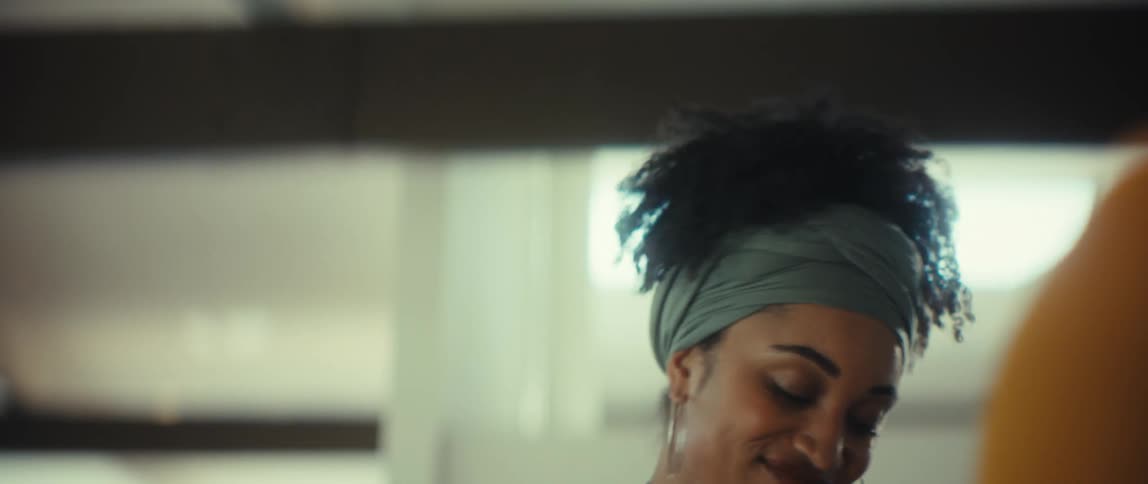 A beautiful woman with a stylish headwrap smiles lovingly as she begins to dance with her partner indoors
