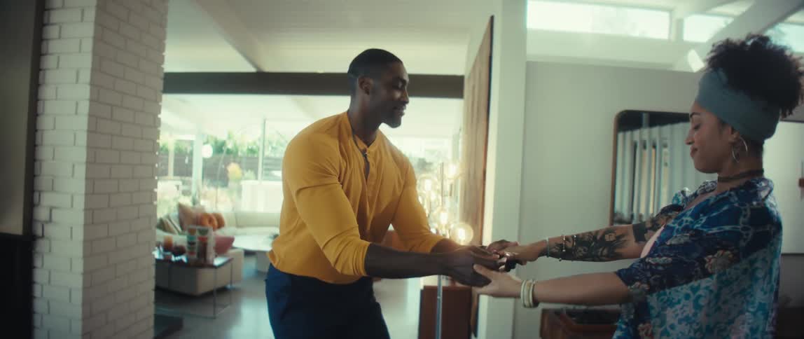 A joyful young couple smiles and dances together in slow motion in their bright, modern living room