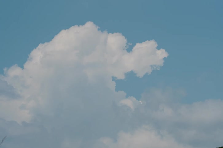 A serene time-lapse captures large, fluffy white cumulus clouds slowly changing shape and dissipating in a vast blue sky