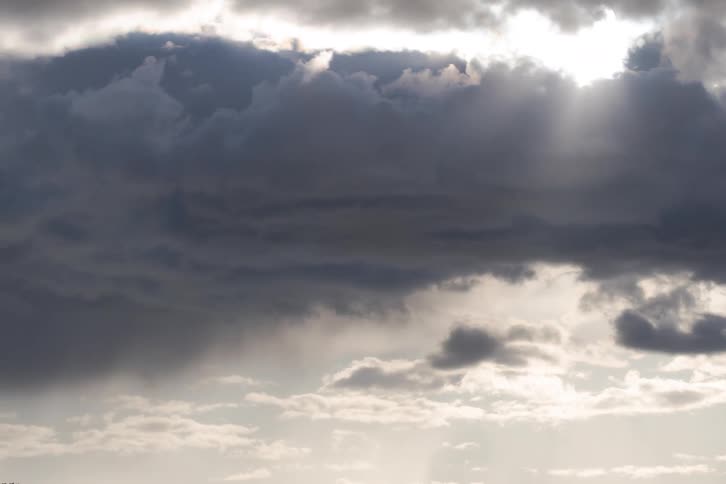 Ominous dark rain clouds drift slowly across the sky as the sun's rays break through the gloom