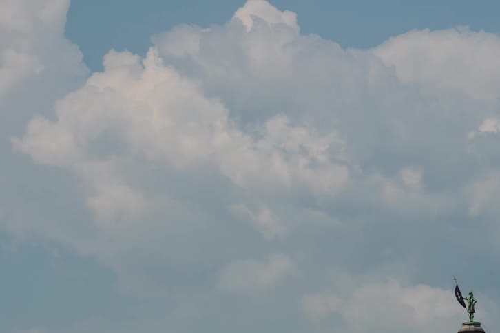 Time-lapse of majestic white clouds drifting across a vibrant blue sky above a historic statue