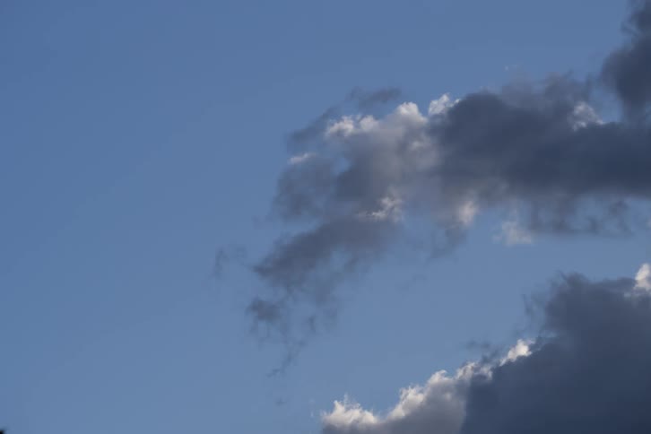 Time-lapse of a shadowy gray cloud formation slowly dissipating against a vibrant blue sky