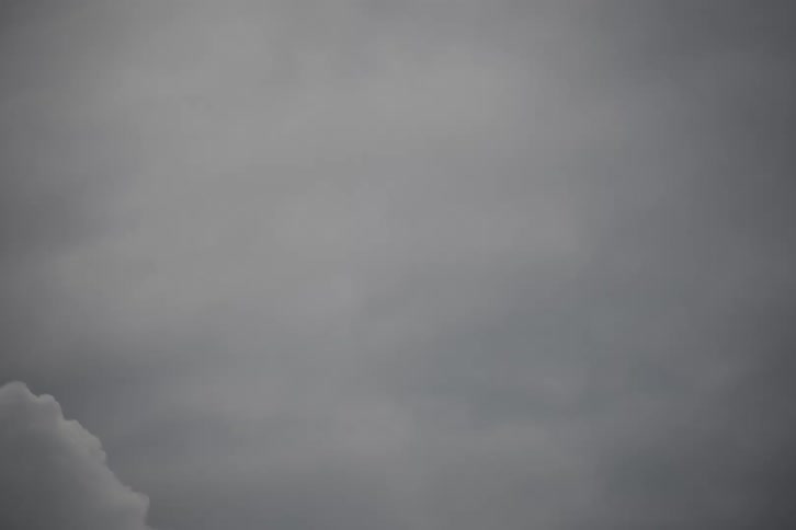 Dense grey clouds slowly drift and dissipate across a gloomy, overcast sky
