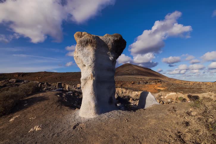 Timelapse of a remarkable white monolith in a volcanic landscape as clouds move across the blue sky