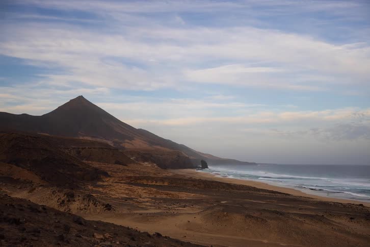 A stunning time-lapse captures a remote volcanic coastline as clouds drift over a mountain peak and waves crash onto a sandy shore