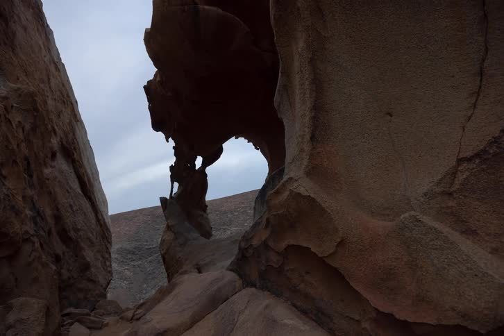 A steady pull-back shot reveals the incredible natural sculpture of an eroded sandstone arch under an overcast sky